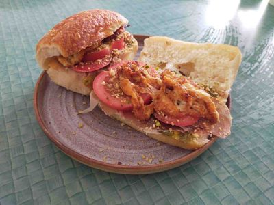 Top-down photo of a ciabatta bun sandwich with pesto, pancetta, tomatoes, dukkah, and fried scamorza on the top