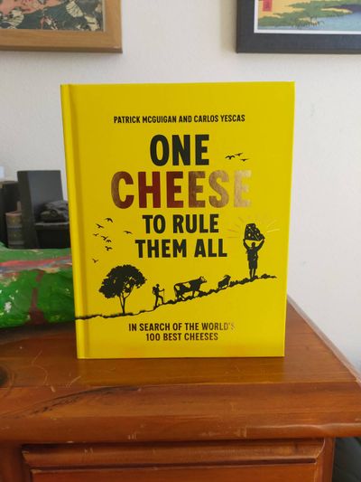 Photo of a book titled 'One Cheese to Rule Them All: In Search of the World'd 100 Best Cheeses' by Patrick McGuigan and Carlos Yescas