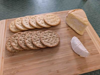 Photo of the smoked brie alongside a small leftover portion of regular value-brand brie and some crackers on a wooden chopping board, layed out like a platter