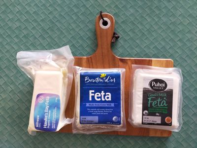 Photo of three wrapped blocks of feta on a chopping board