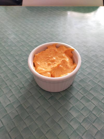 A photo of a ramekin of orange-red tirokafteri dip sauce