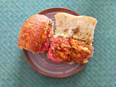 Side-on photo of a ciabatta bun sandwich with pesto, pancetta, tomatoes, dukkah, and fried scamorza on the top