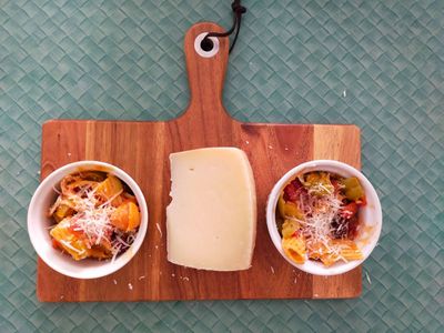 A photo of unwrapped pecorino on a cheese board alongside two small ramekins of pasta with pecorino grated on them