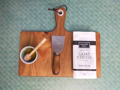 A photo of wrapped goat cheese on a chopping board alongside a pottle of honey.